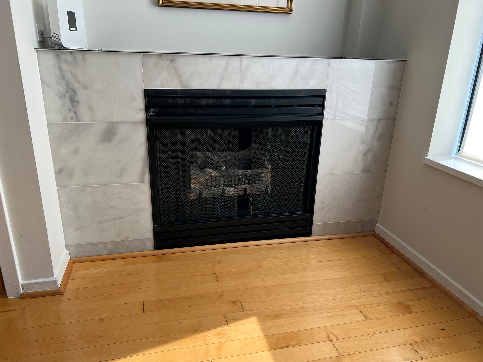 Fireplace with black grate, white marble surround, and light wood floor.