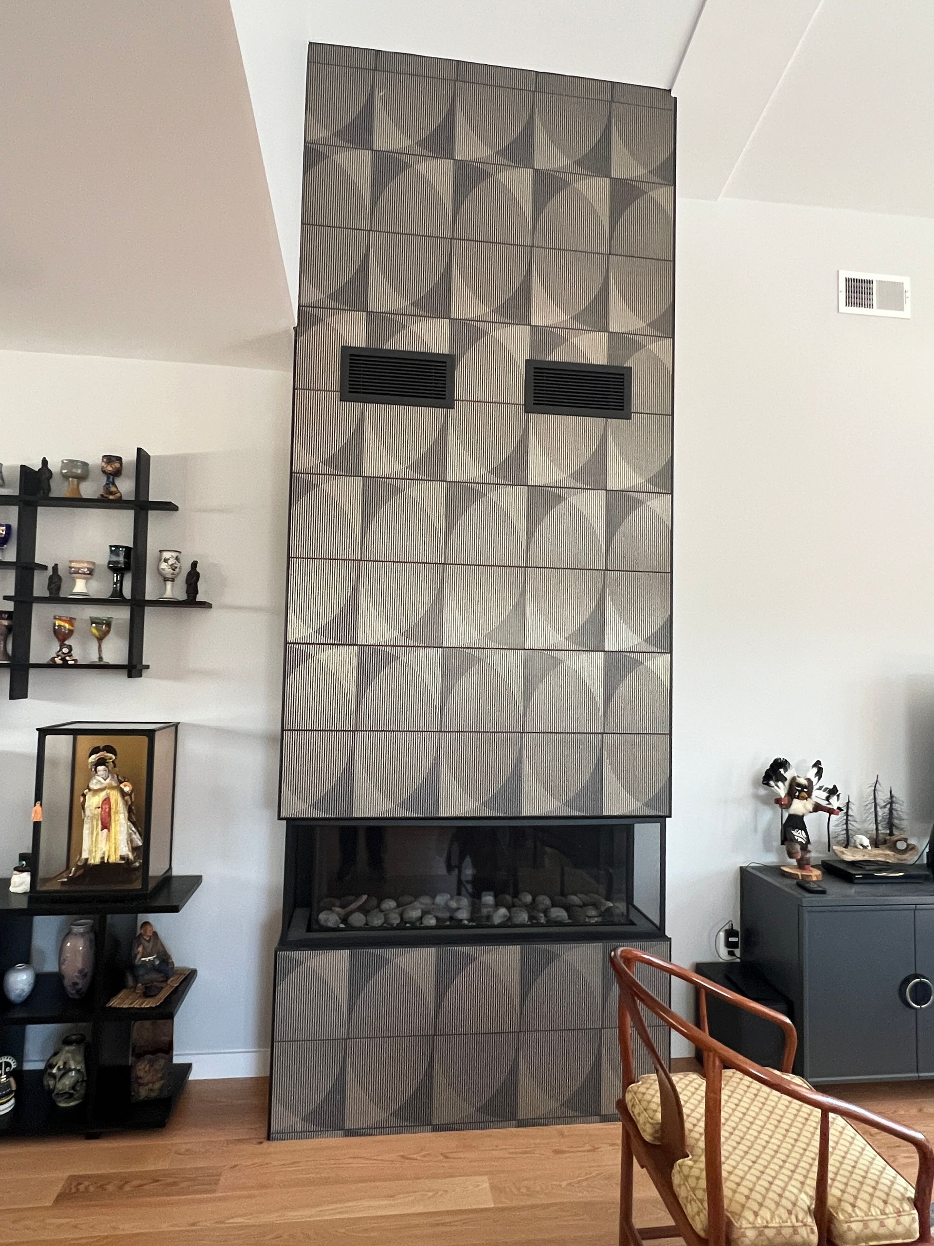 Modern fireplace with textured paneling and black vents, flanked by furniture and decor.