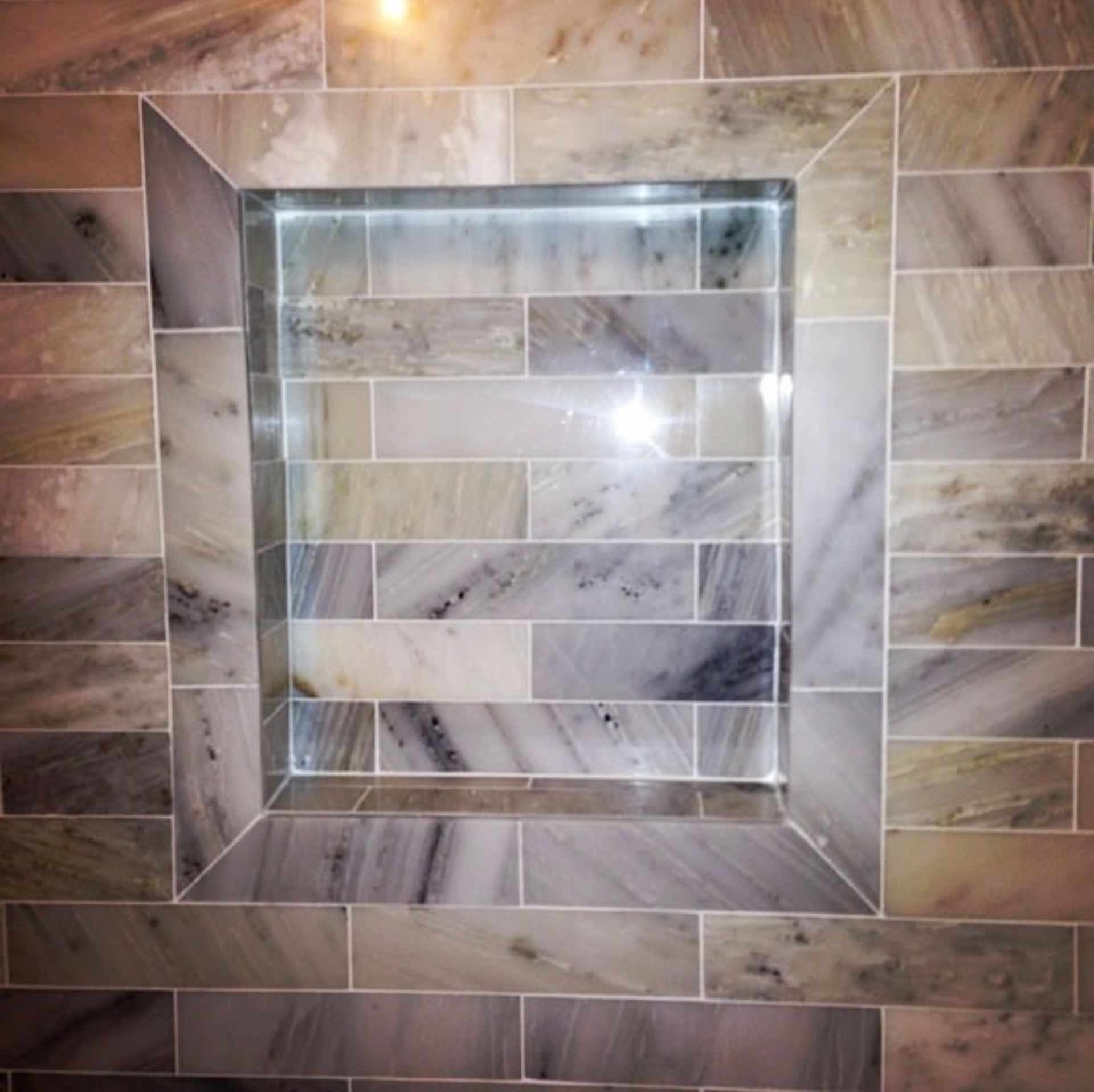 Shower niche with rectangular tiles, marble pattern, illuminated, set into tiled wall.
