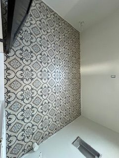 Patterned tile wall with a floral design, contrasted against a white wall.