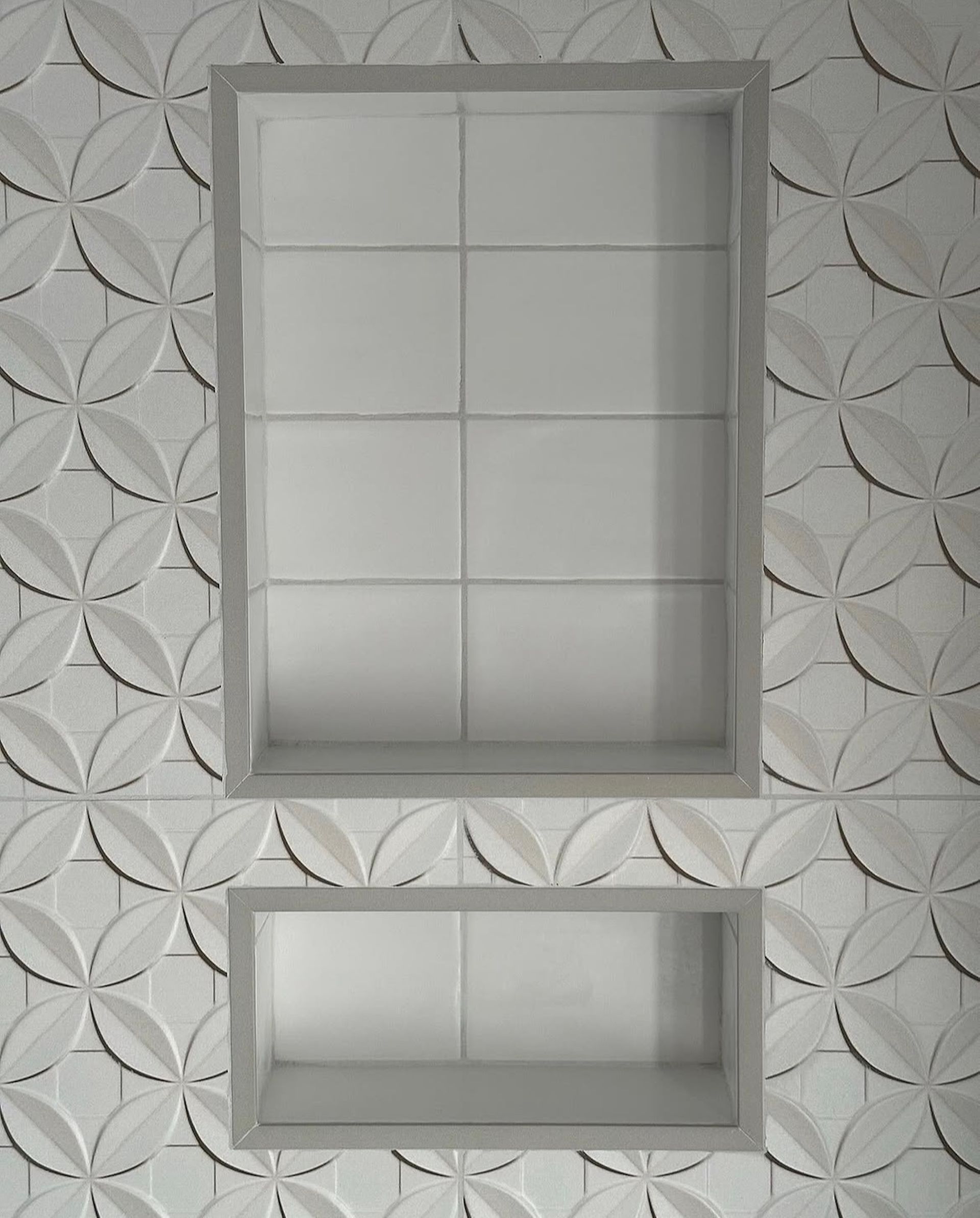 Two recessed, tiled shelves in a bathroom wall with a patterned, white tile background.