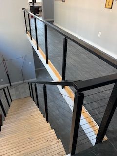 Staircase with black railing and gray flooring, leading down from a second-floor area.