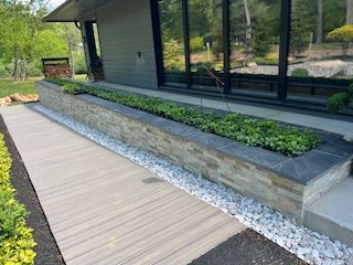 Gray and stone planter box with greenery, alongside a composite walkway and building with dark windows.