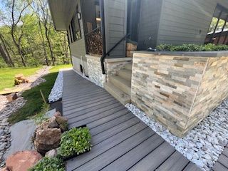 Grey composite ramp leading to a house with stacked stone facade and landscaping.