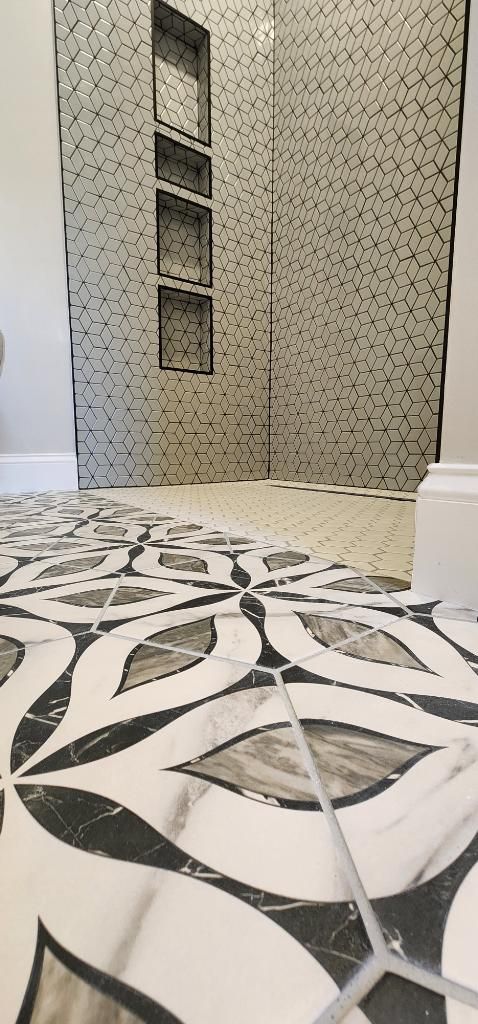 Bathroom with patterned floor tiles leading to a mosaic-tiled shower with recessed shelving.