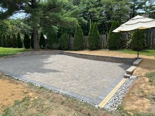 Brick patio in backyard with stone retaining walls, umbrella, and trees.
