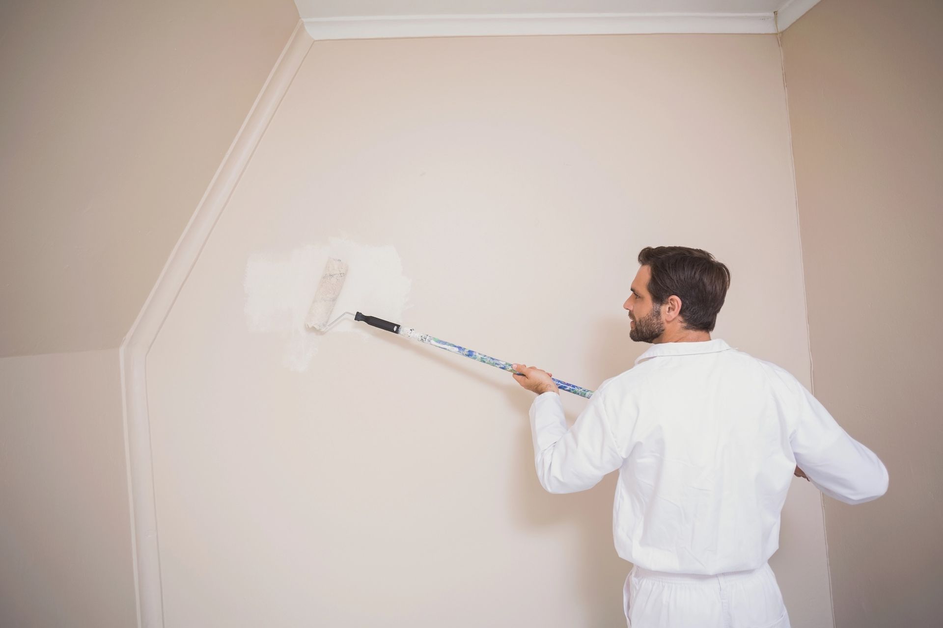 Person in white overalls painting a wall with a roller.