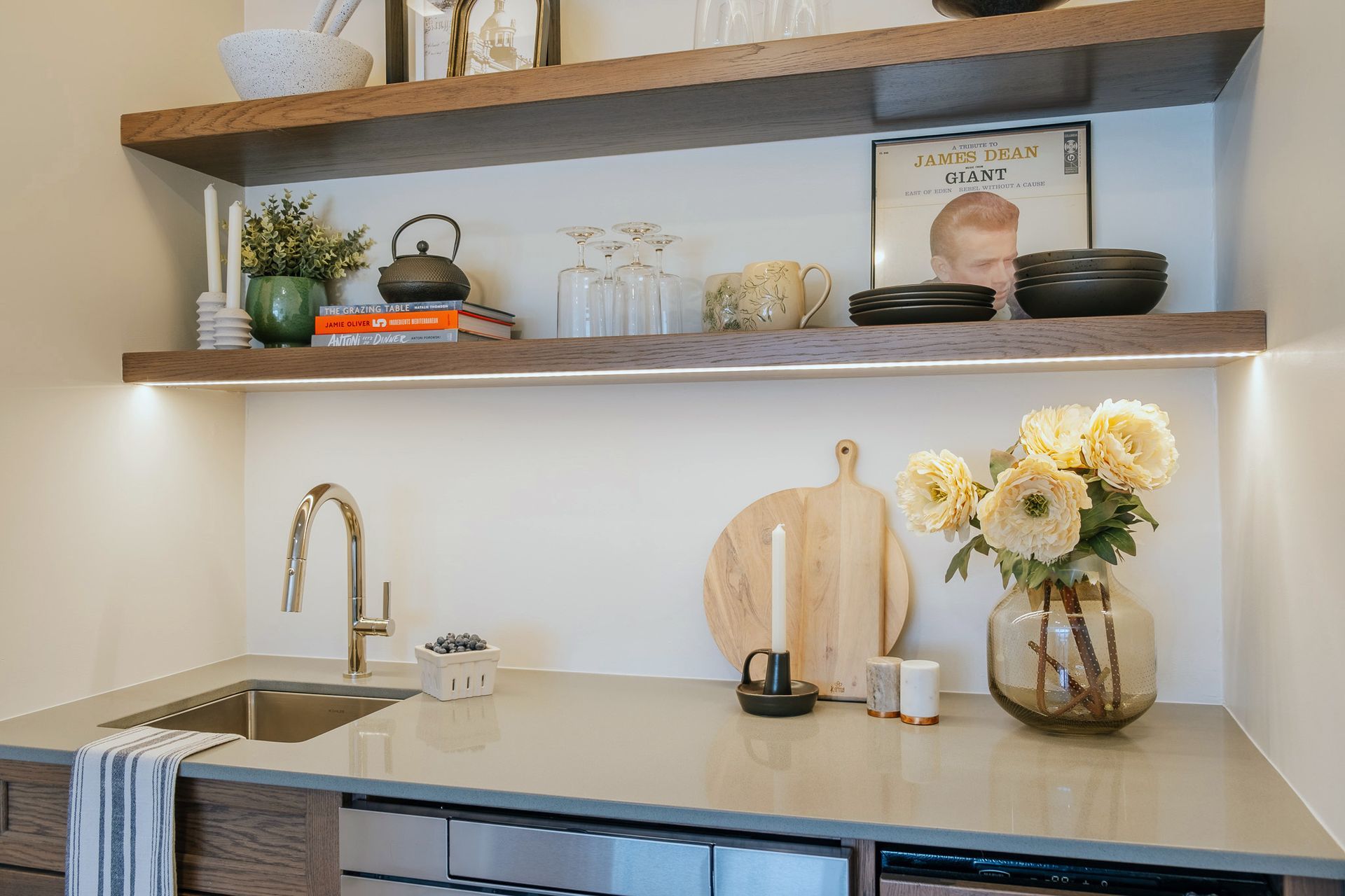 A kitchen with a sink, shelves, and a vase of flowers on the counter.