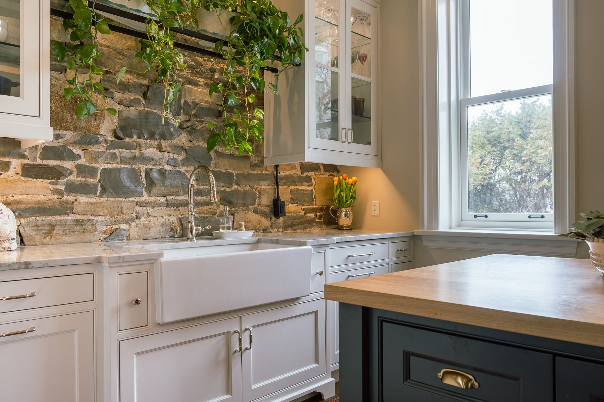 A kitchen with a sink, cabinets, and a stone wall.
