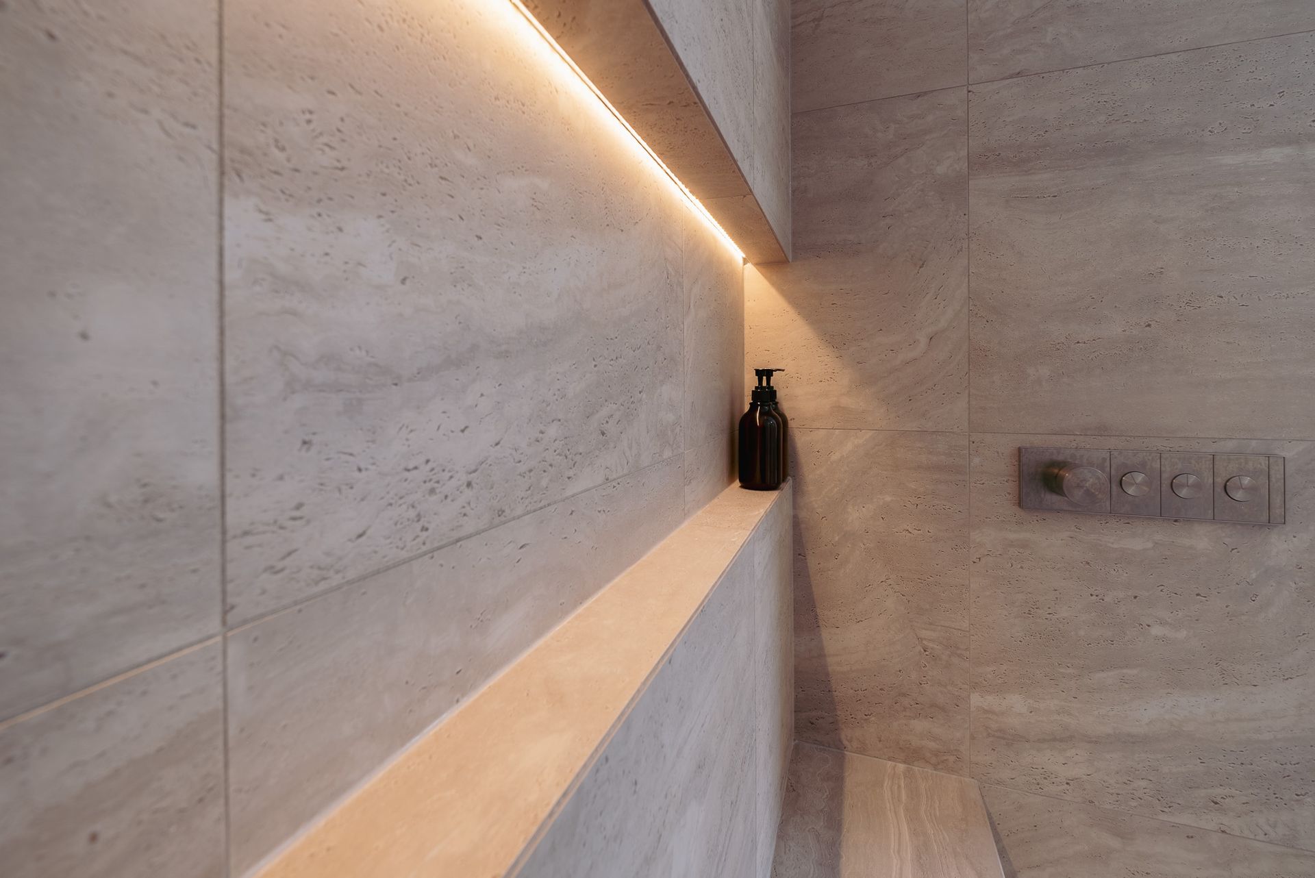 A soap dispenser on the shelf in the shower.
