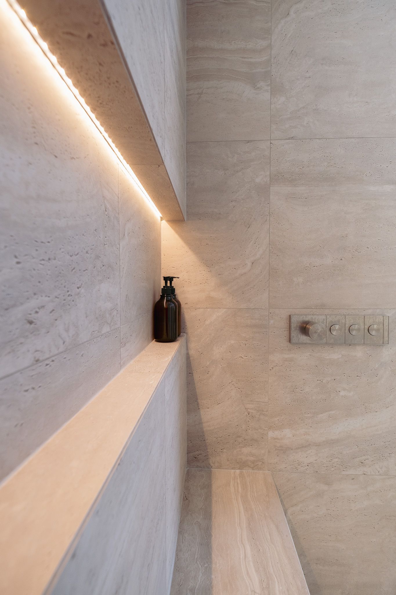 A bottle of soap sitting on a shelf in a bathroom next to a shower.