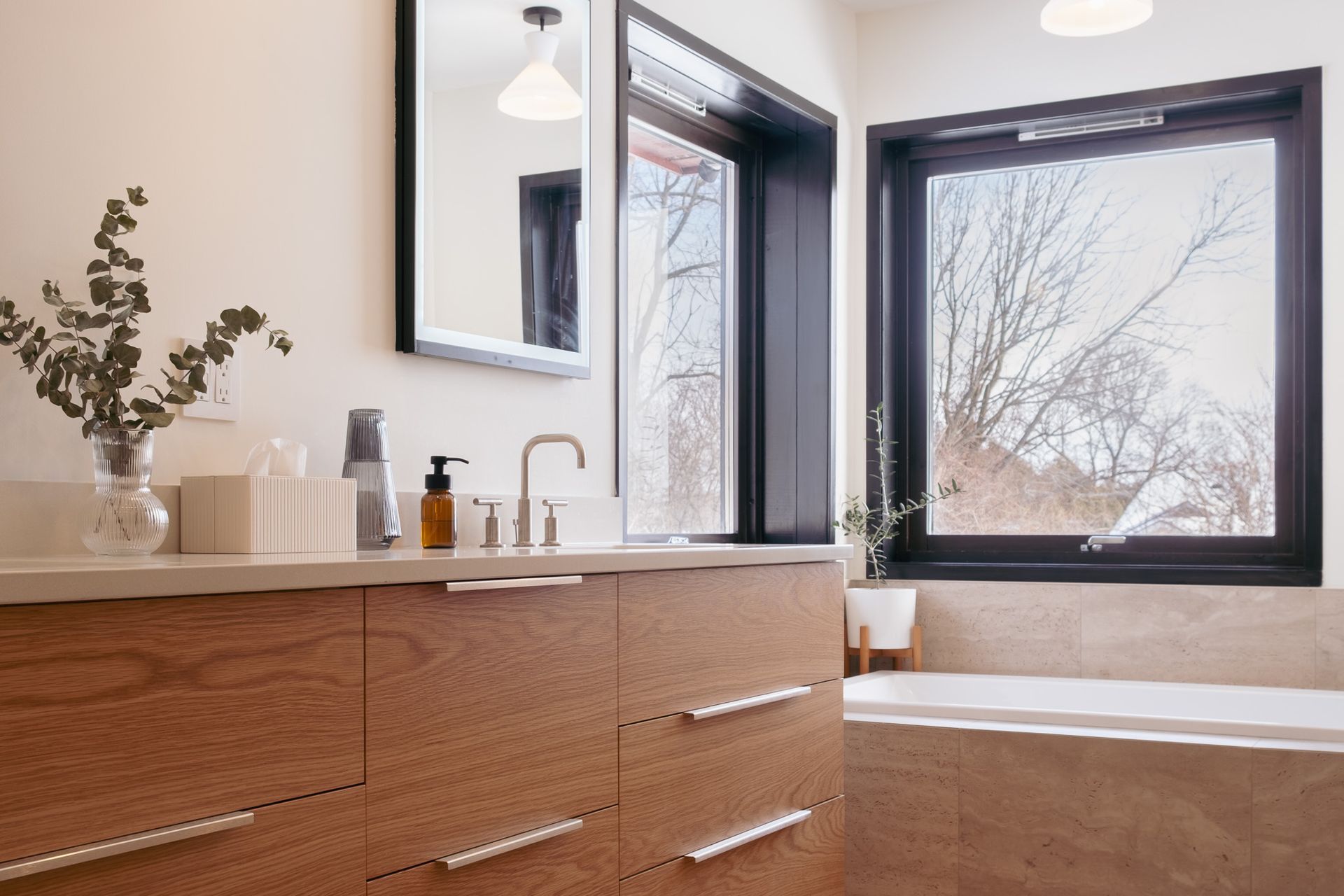 A bathroom with a sink, mirror, tub and window.