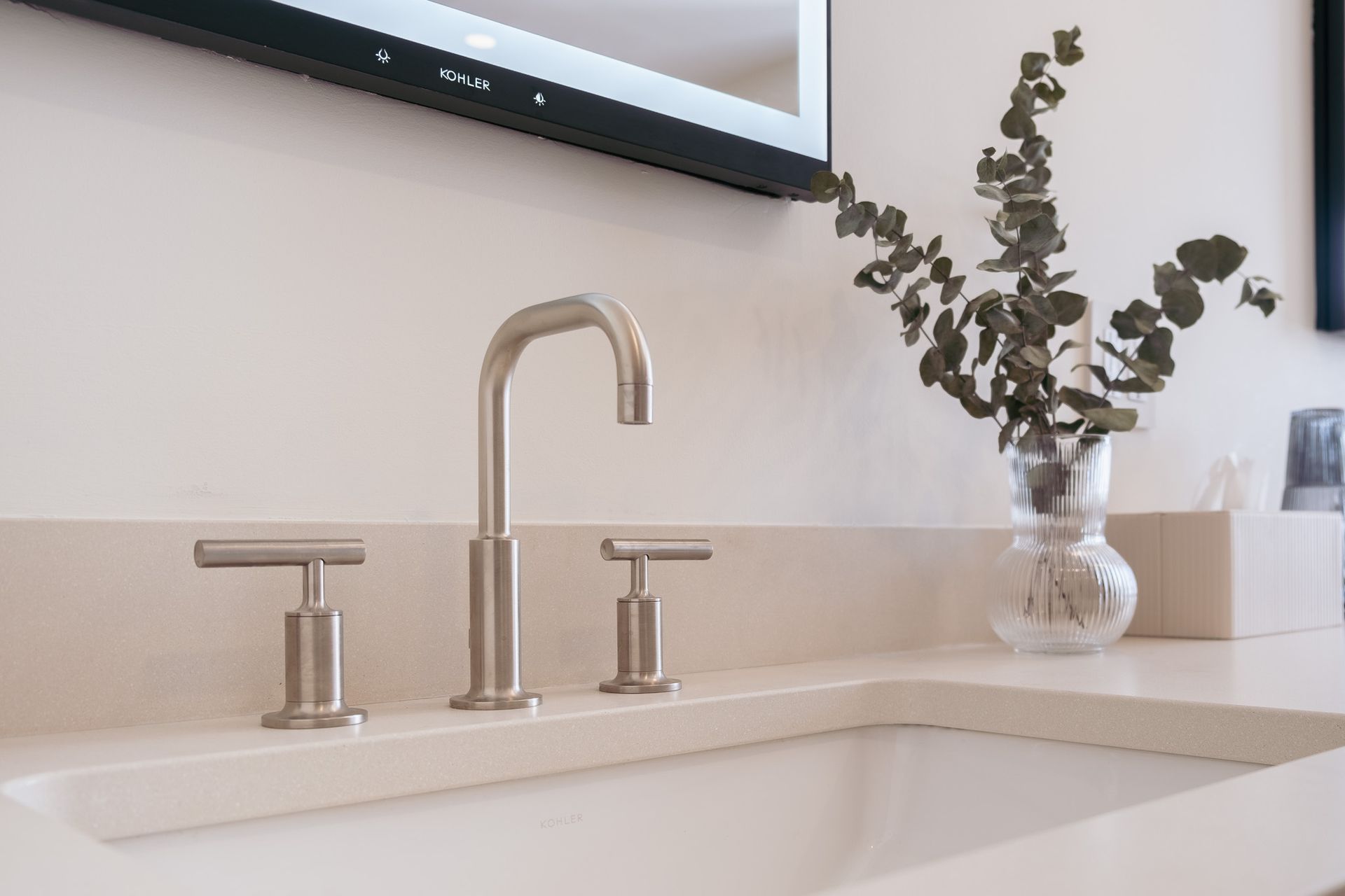A bathroom sink with a faucet and a vase of flowers on the counter.