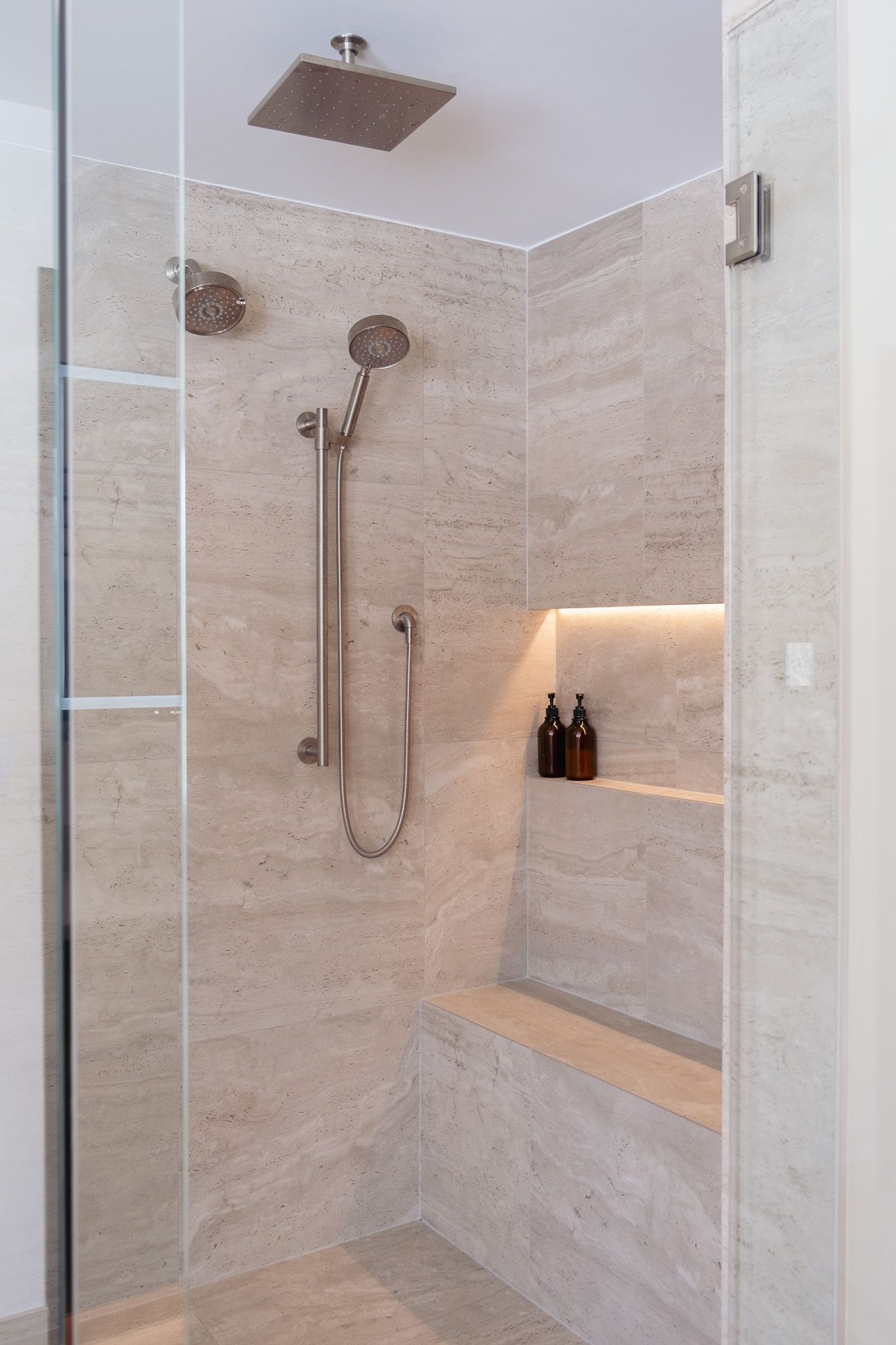 A bathroom with a walk in shower with a glass door and a shelf.