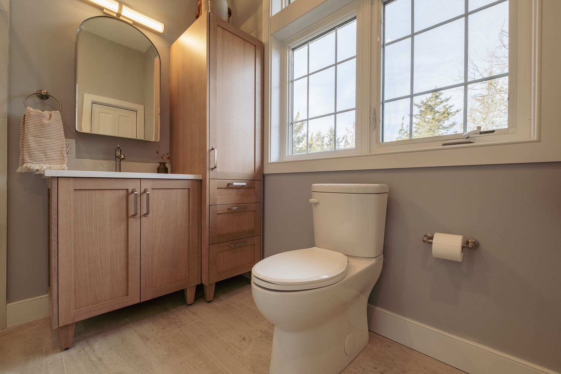 A bathroom with a toilet, sink, mirror and window.