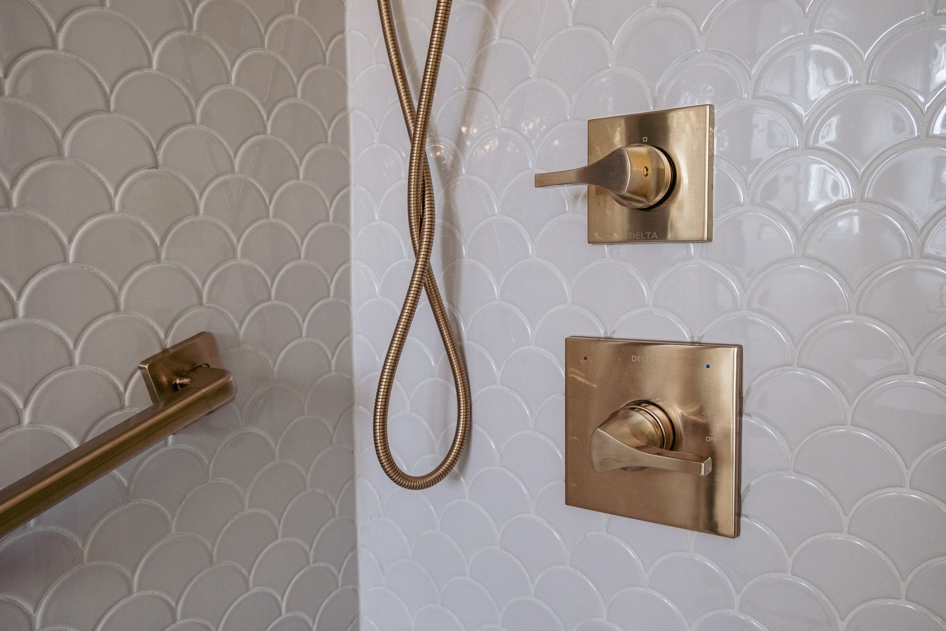 A bathroom with white tiles and gold shower faucets.