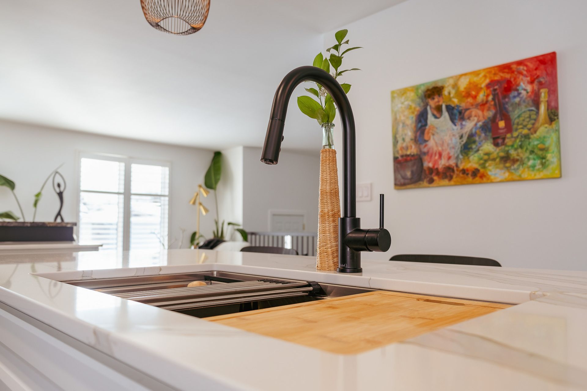 A kitchen sink with a black faucet and a painting on the wall behind it.