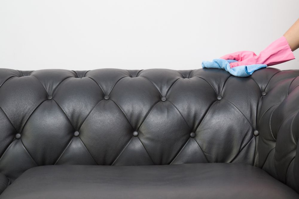 A Person is Cleaning a Black Leather Couch With a Cloth — Carpet Pro Care in Goonellabah, NSW