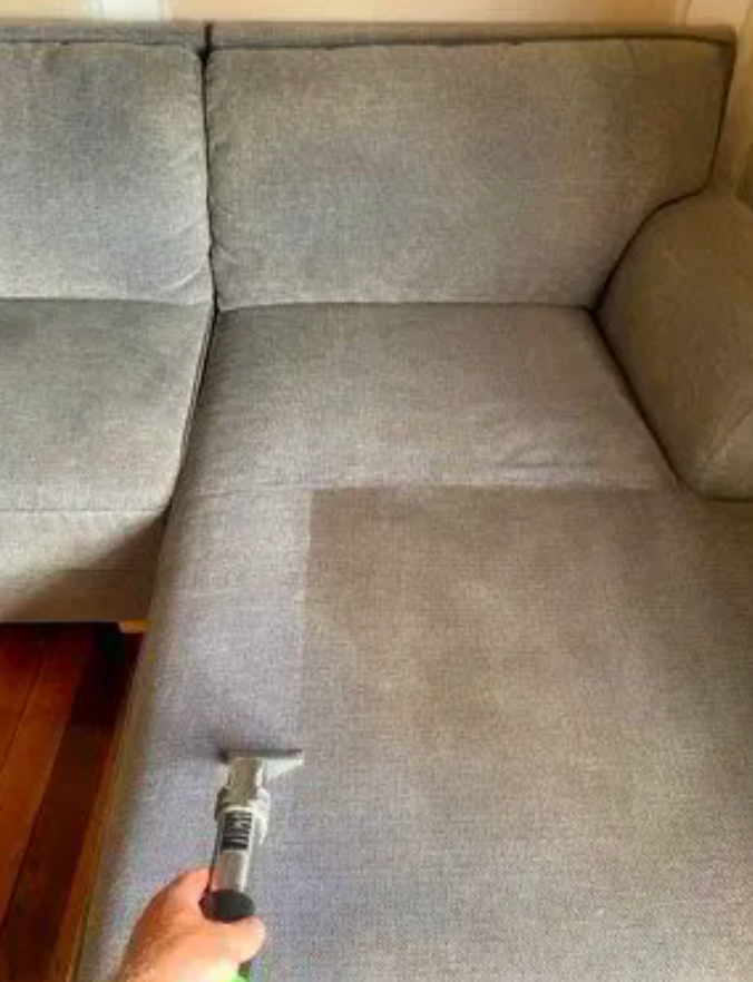 A Man is Cleaning a Couch With a Vacuum Cleaner And Half Is Cleaned And Half Dirty — Carpet Pro Care in Goonellabah, NSW