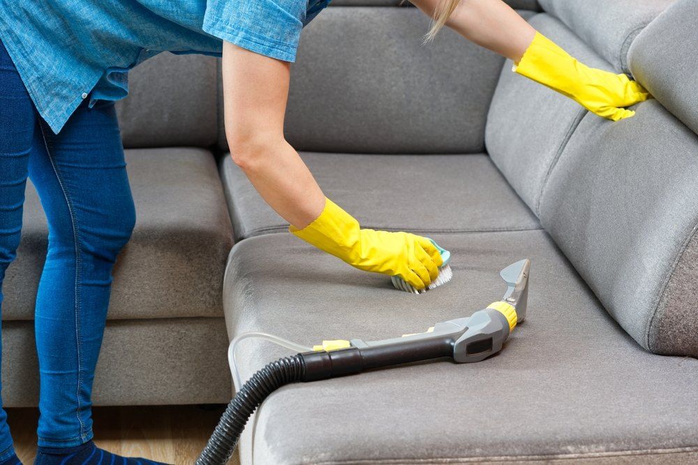 A Woman is Cleaning a Couch With a Vacuum Cleaner — Carpet Pro Care in Kyogle, NSW
