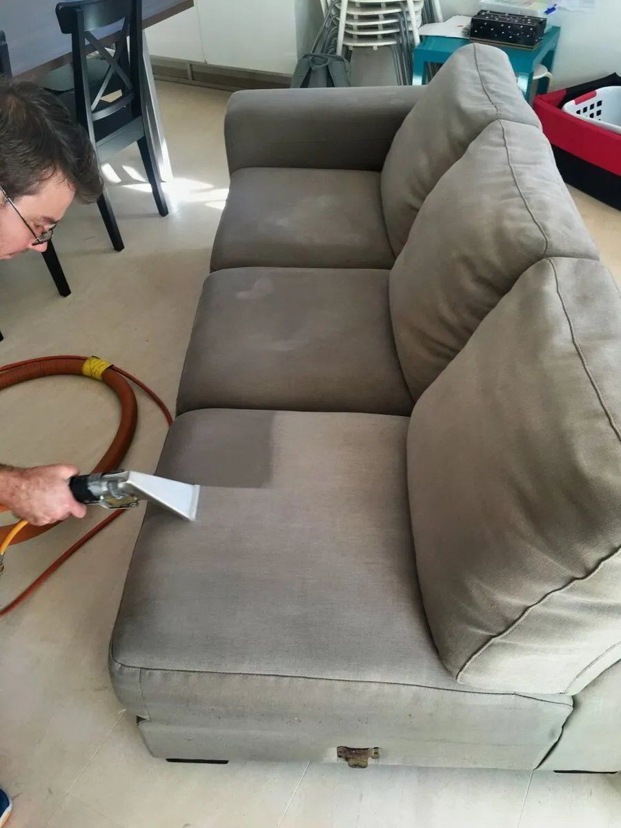 A Man is Cleaning a Couch With a Vacuum Cleaner — Carpet Pro Care in Goonellabah, NSW