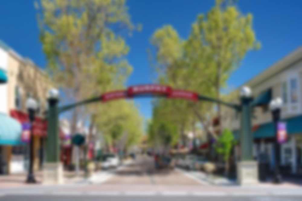 Tree-lined pedestrian street with a red archway between buildings on a sunny day
