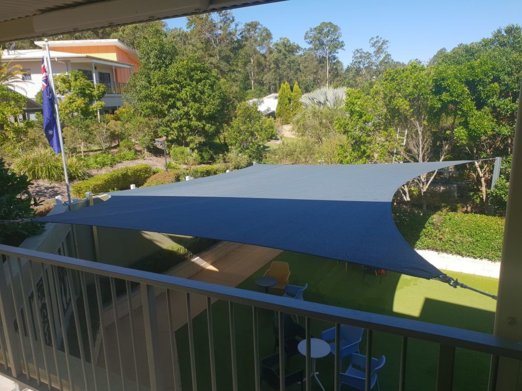 A Large Blue Umbrella is Sitting on a Balcony Overlooking a Lush Green Yard — Cooloola Sail Company In Pomona, QLD