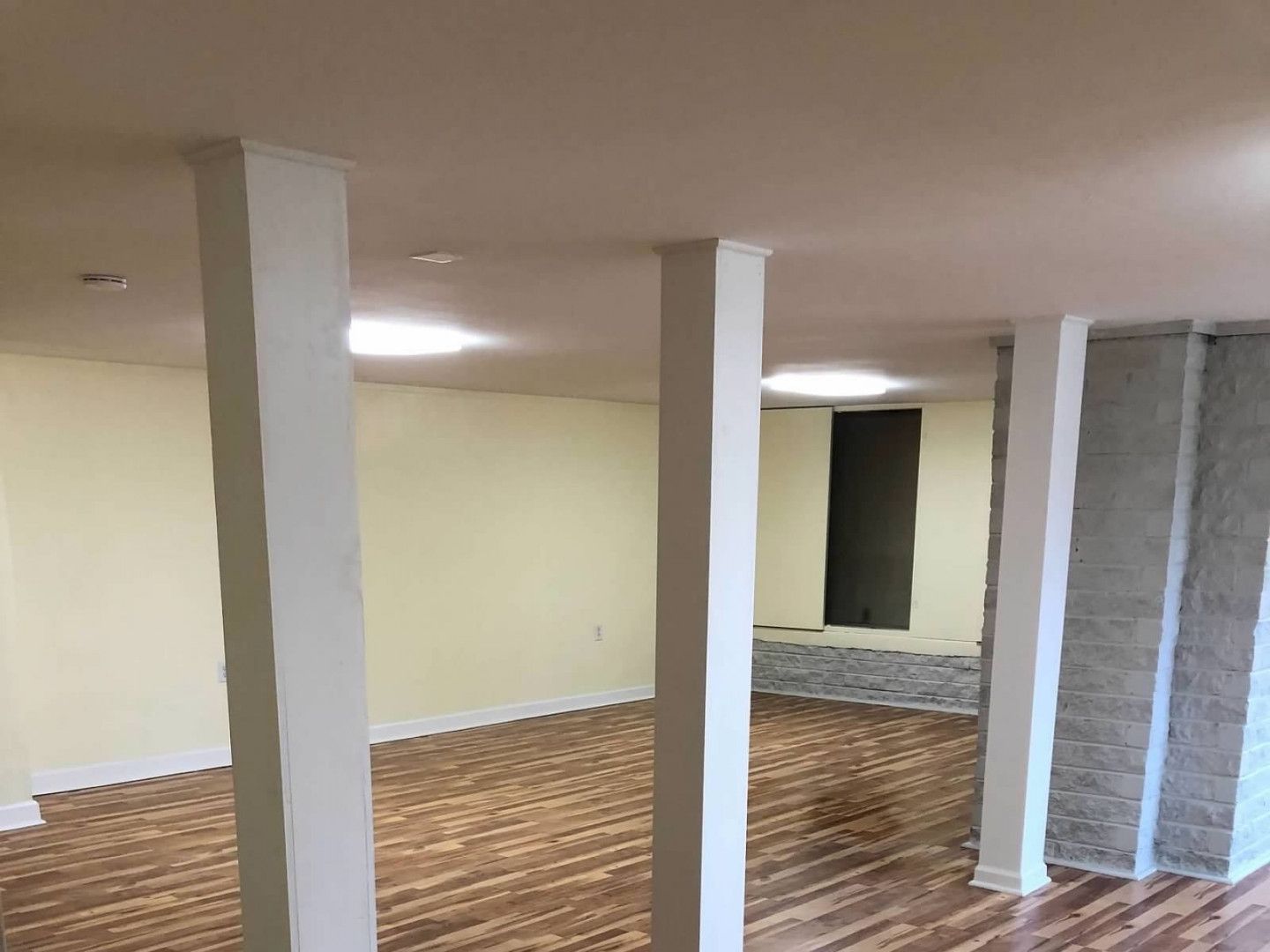 A basement remodeled with gorgeous columns and hardwood floors using contrasting wood colors by Compass Construction