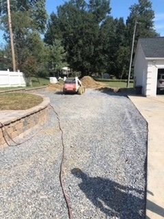 A car is parked in a gravel driveway next to a garage.