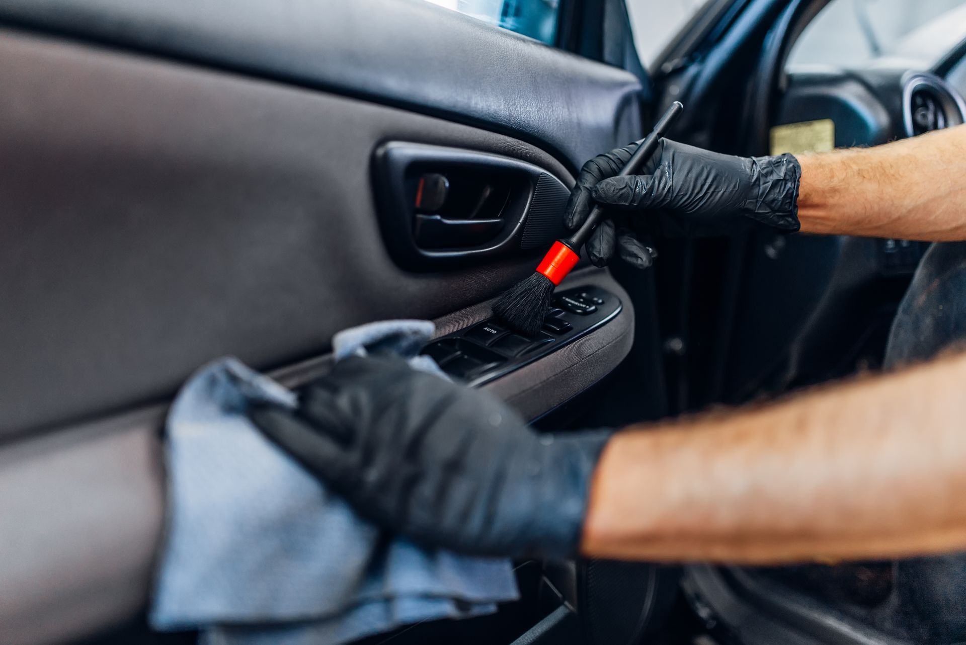 Black-gloved hands using a red pry tool to open a car door from inside