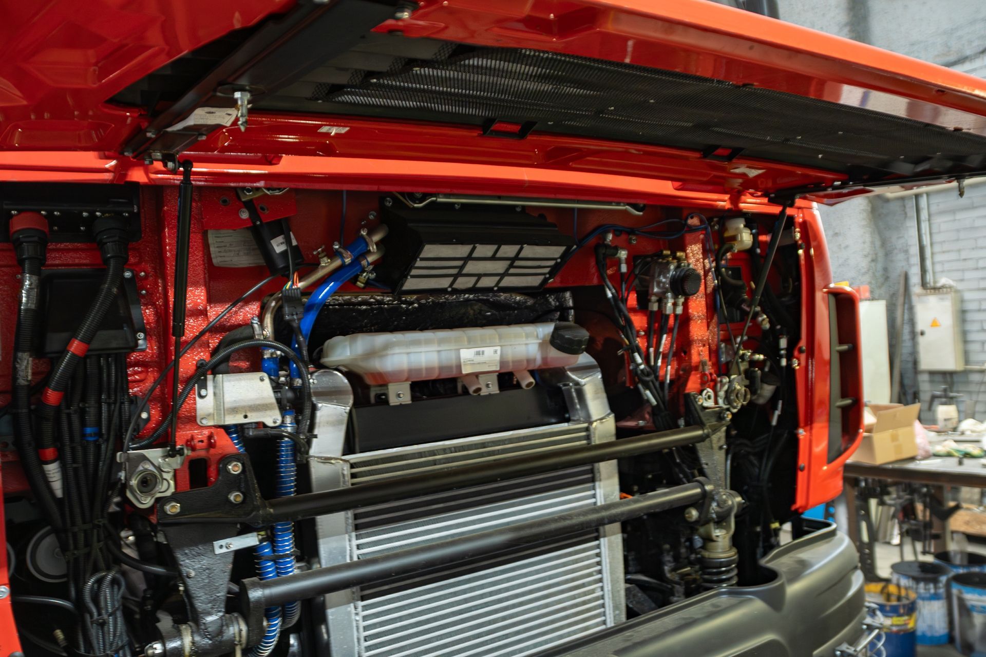 Red vehicle engine bay with exposed components and a large rear radiator, viewed from the open back.