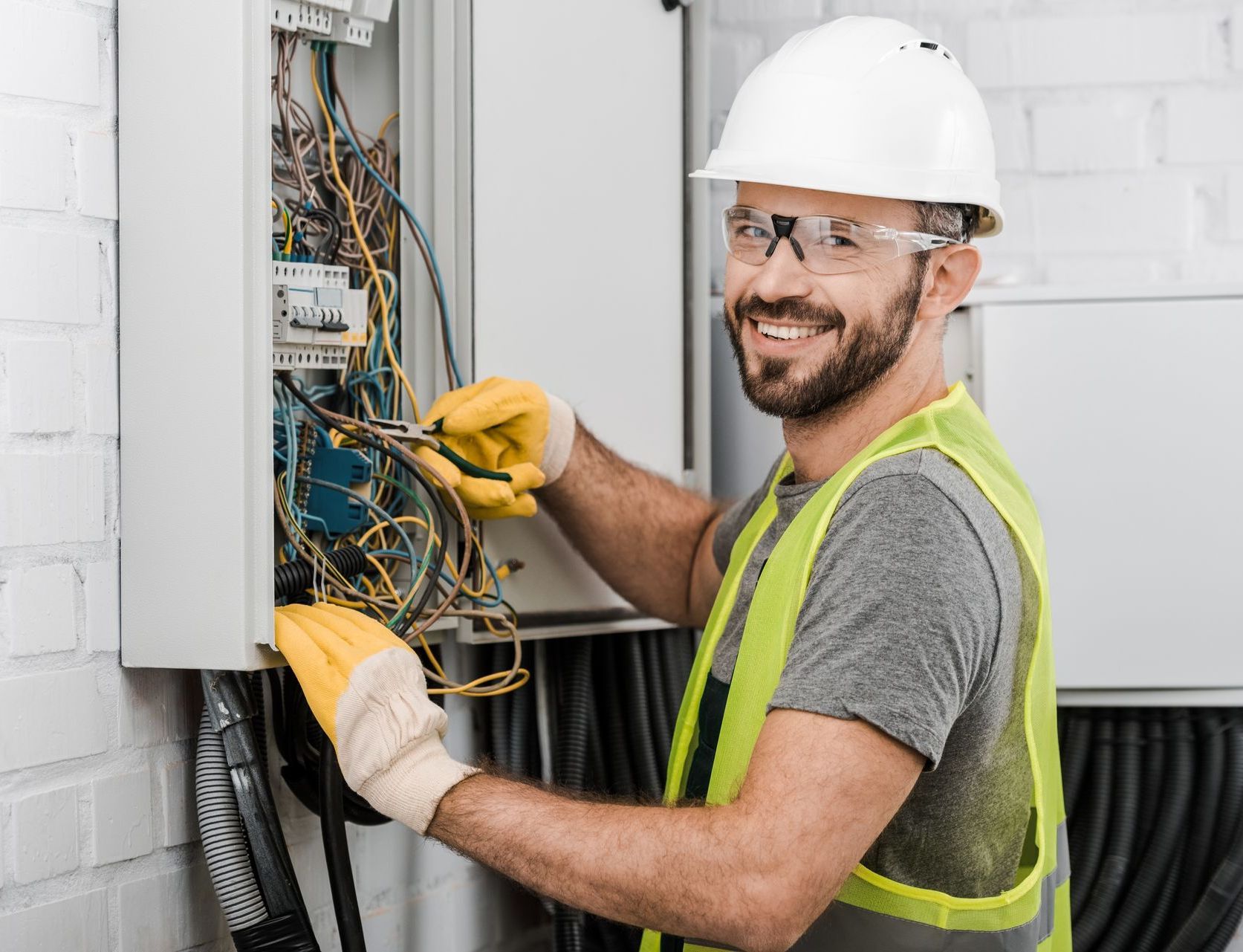 Technicien portant un casque et un gilet de sécurité, effectuant le câblage d'un tableau électrique avec des gants jaunes