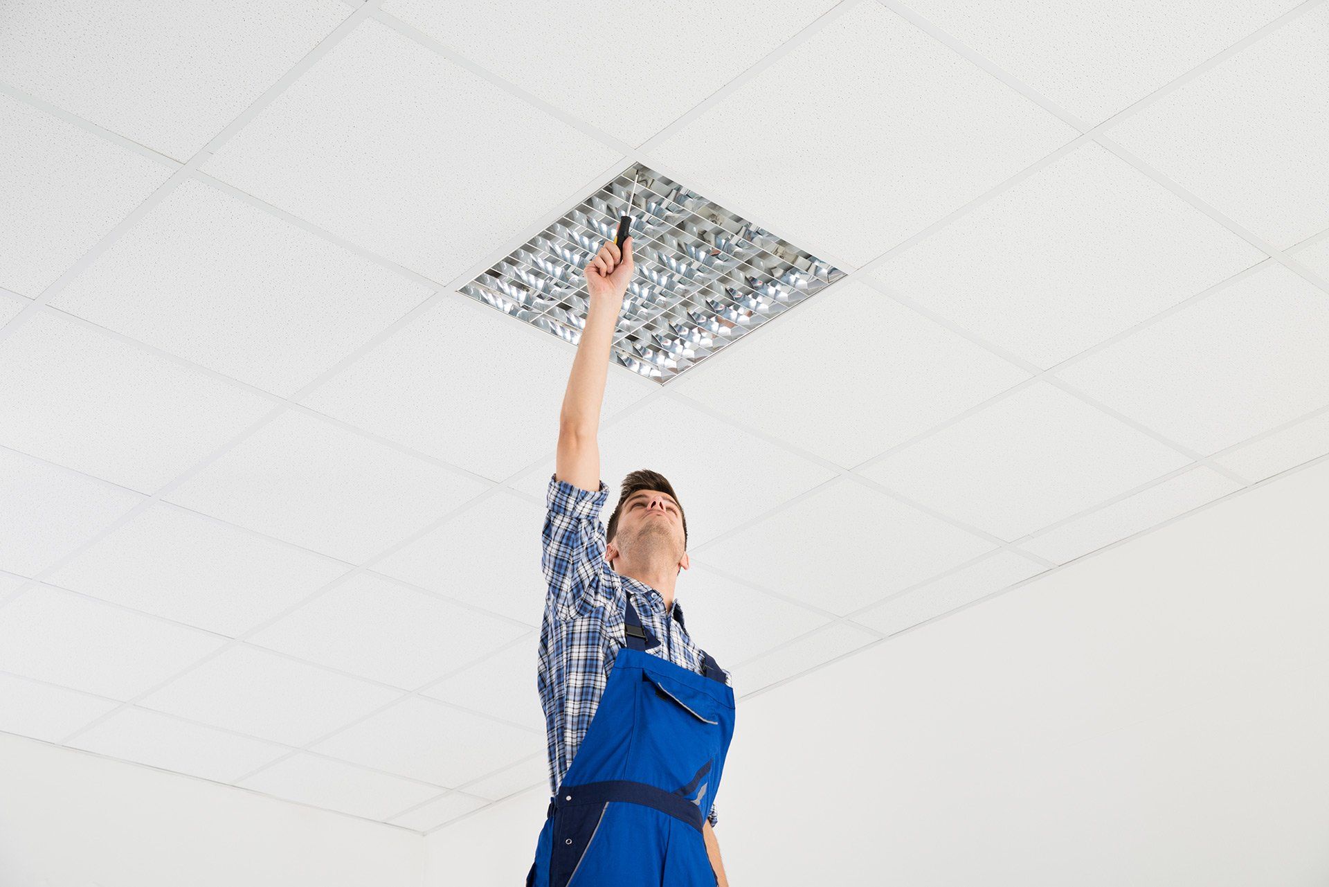 Un homme fixe un luminaire au plafond.