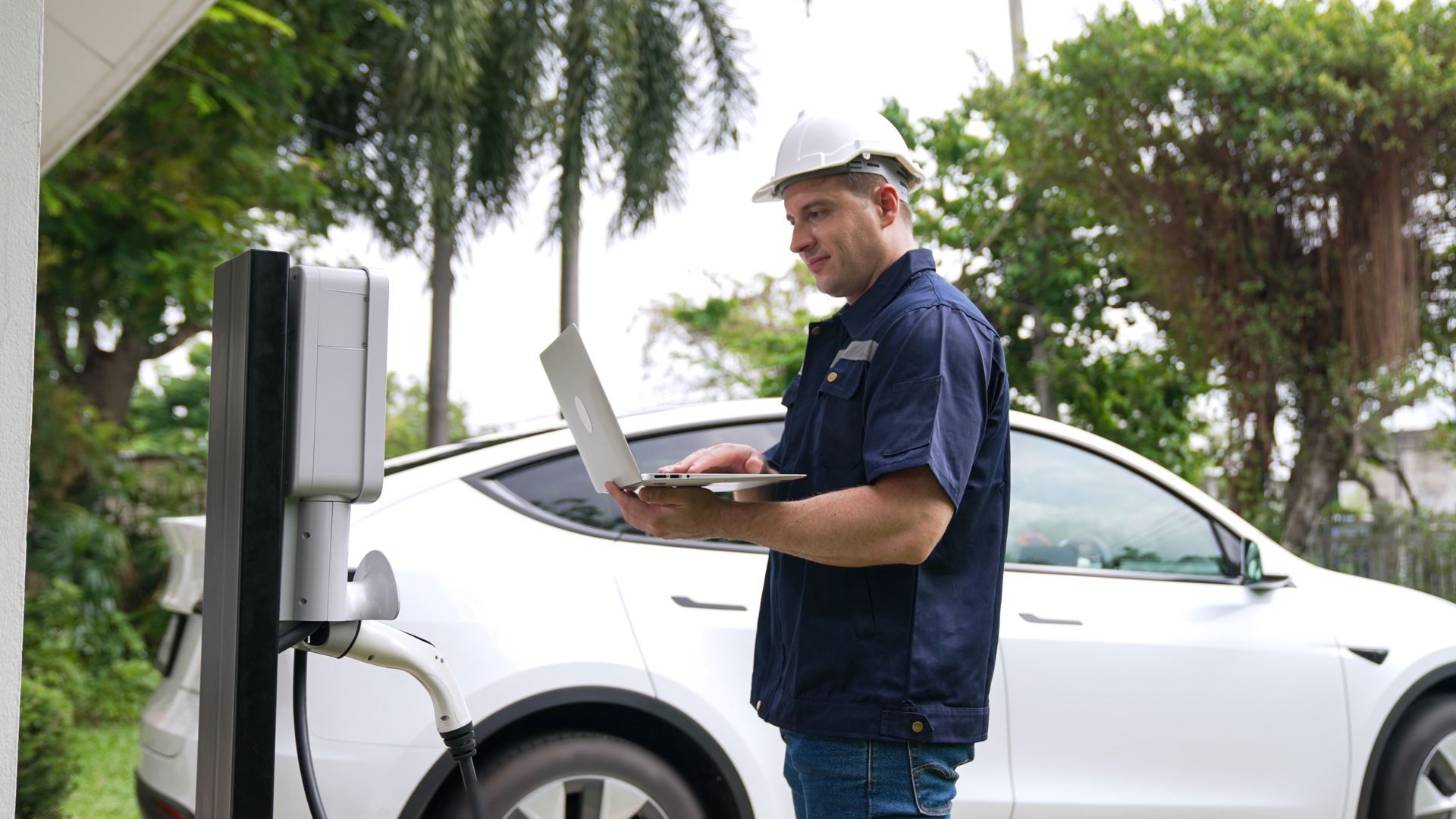 Un homme utilise un ordinateur portable tout en chargeant une voiture électrique.