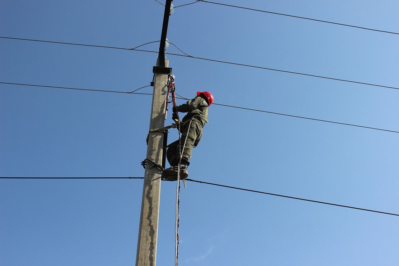 Un homme portant un casque rouge grimpe sur un poteau électrique.