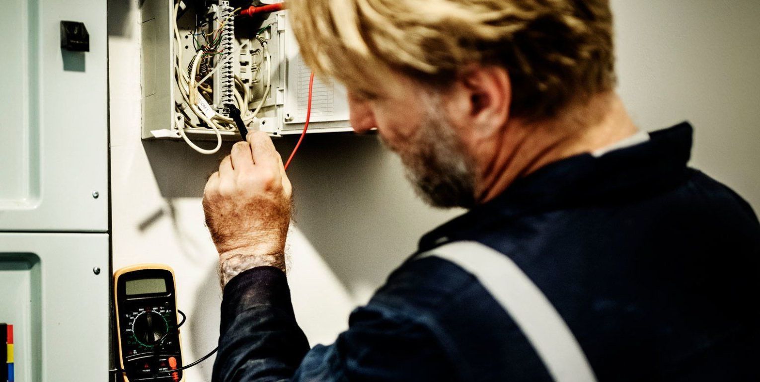 Un homme travaille sur un coffret électrique avec un multimètre.