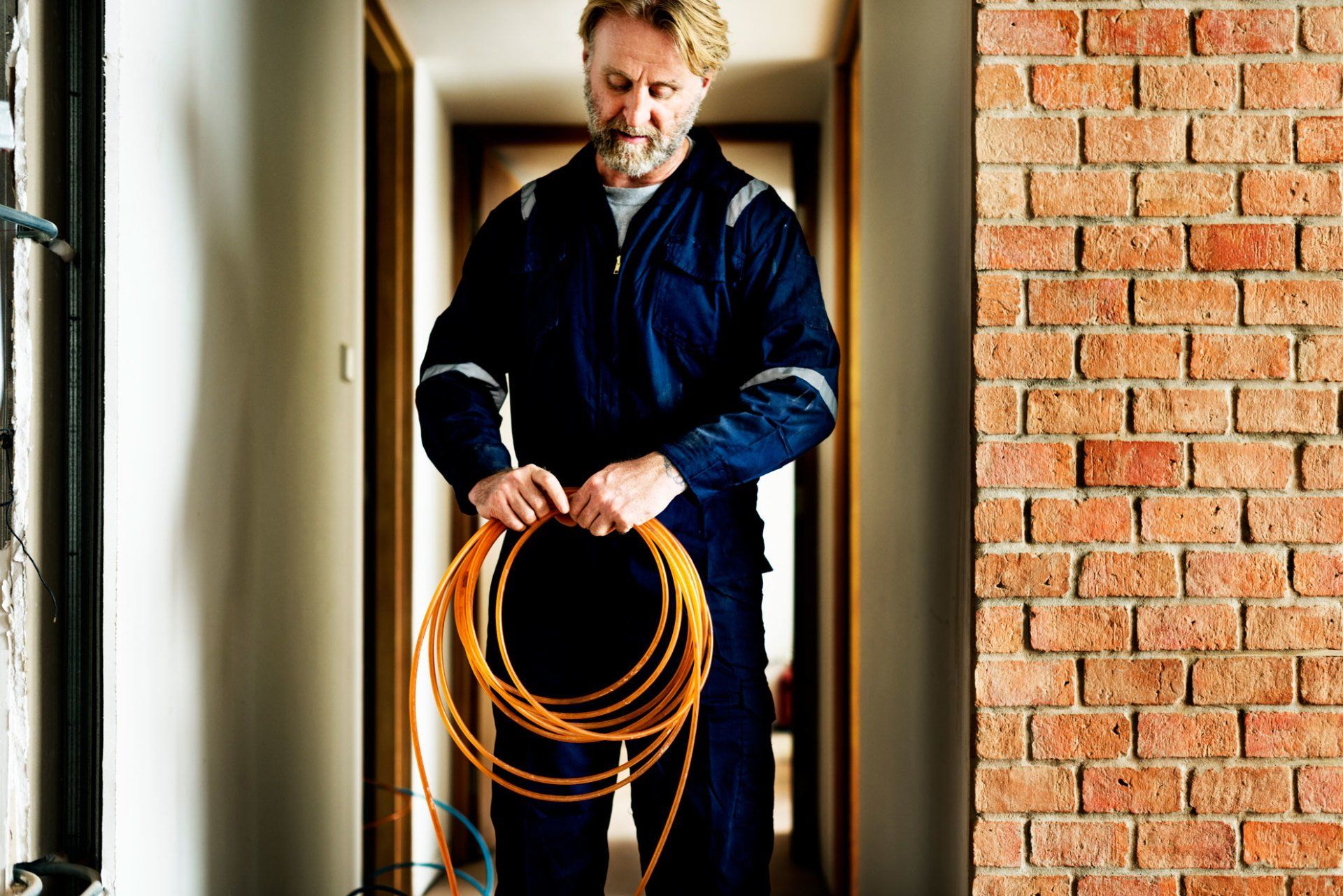 un homme tient une bobine de fil orange dans un couloir.