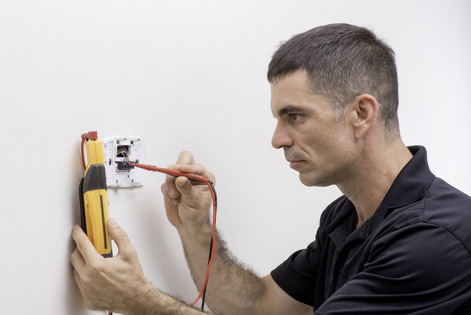 Man testing an electrical outlet with a multimeter beside a wall-mounted box