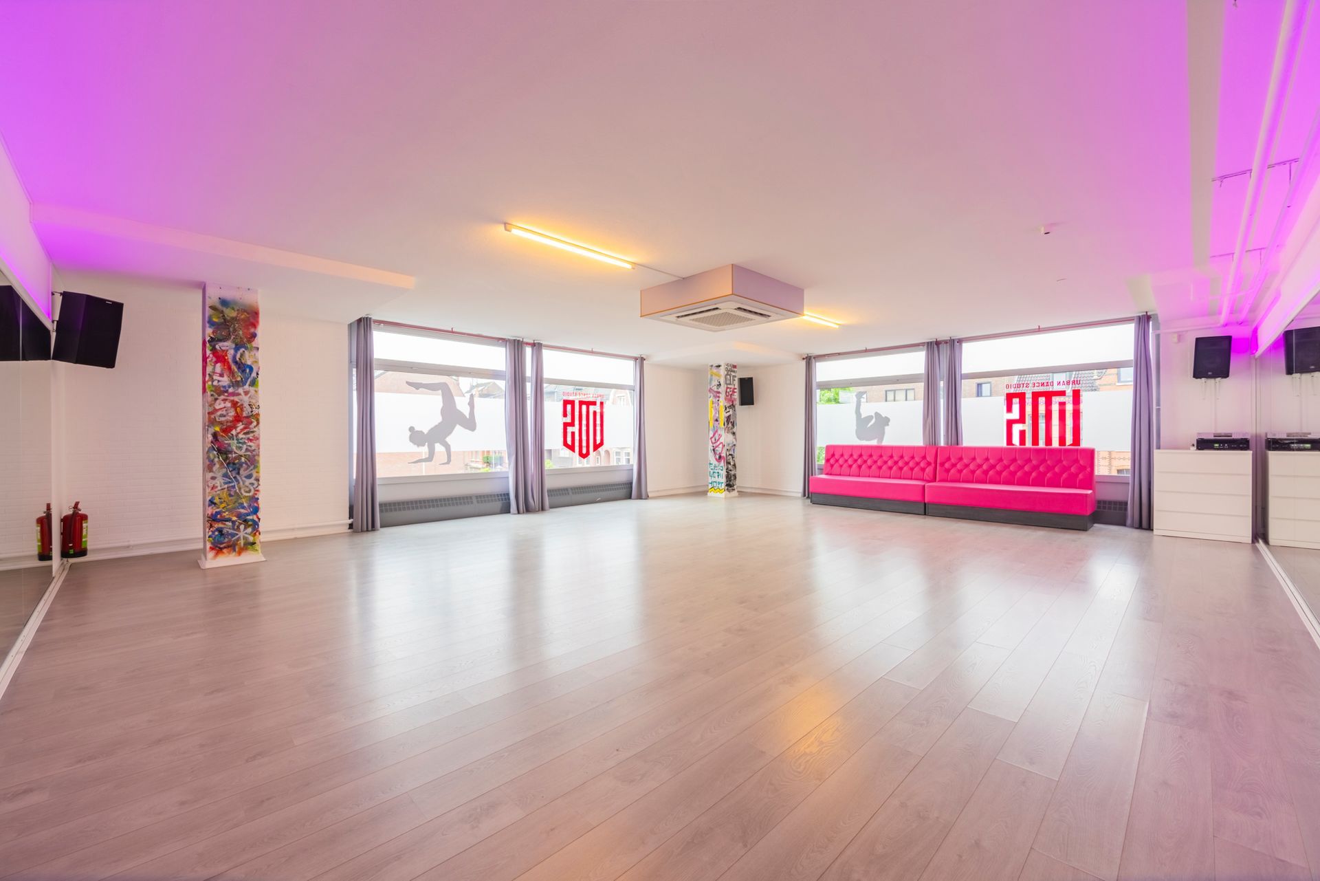 Ruime, lege, moderne studio met lichte houten vloeren, roze verlichte muren en grote ramen.