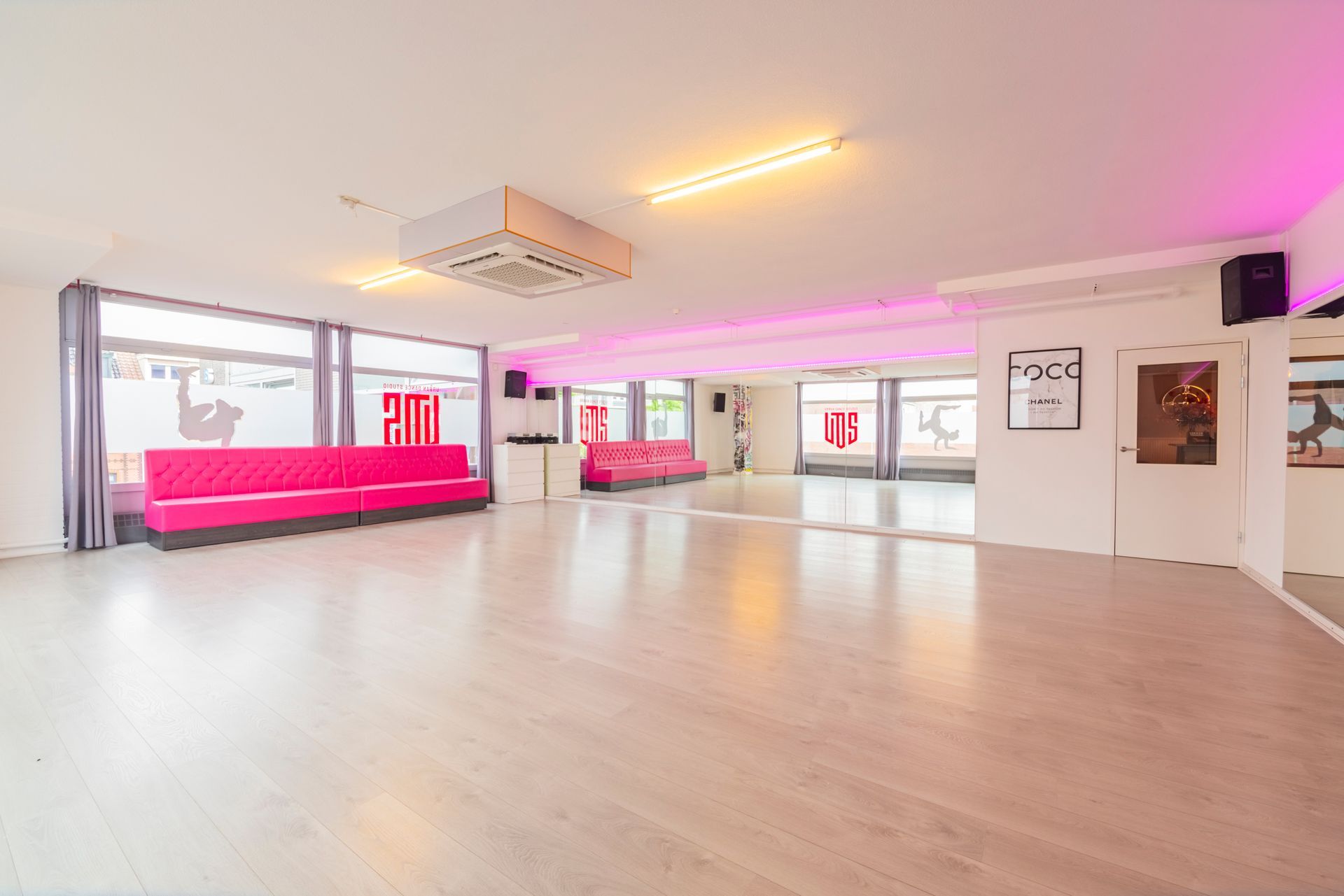 Een felroze lounge met grote ramen, houten vloer en plafondlampen in een moderne, studio-achtige ruimte.