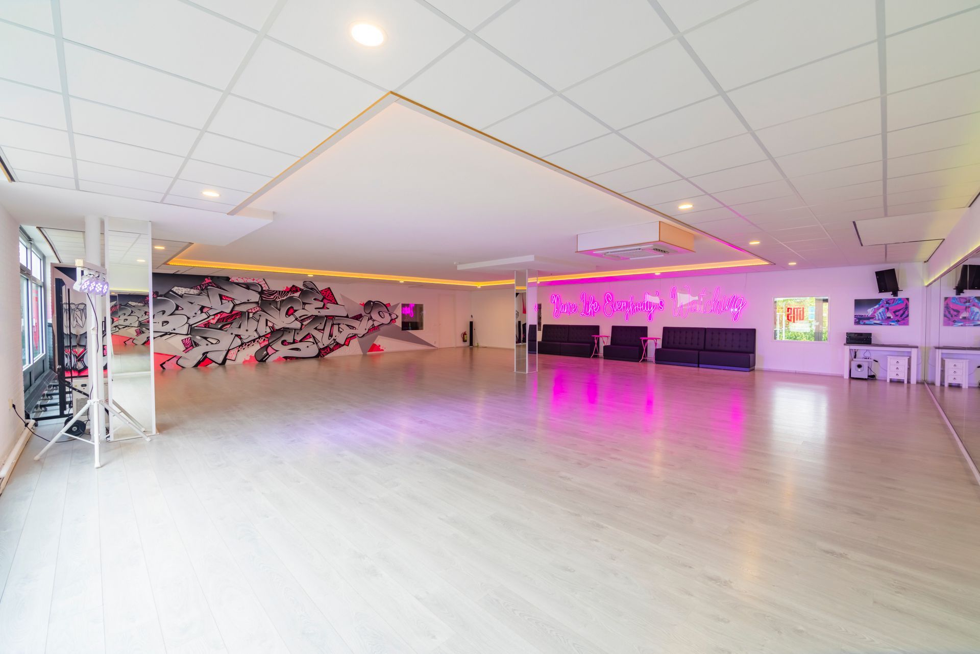 Ruime, lege dansstudio met roze verlichting, spiegelwand en gepolijste houten vloer.