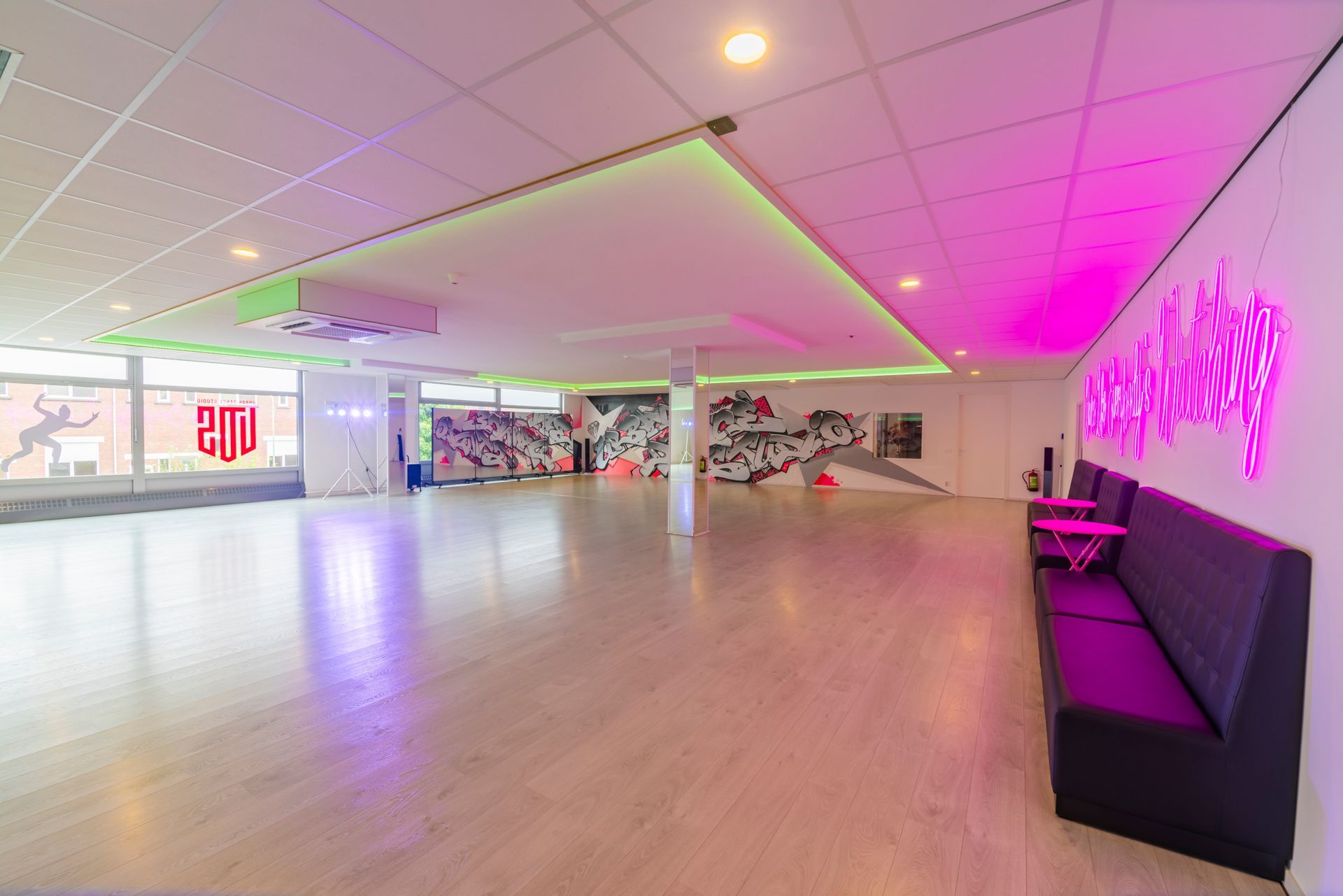 Een lege, moderne lobby met roze neonverlichting, houten vloeren en zwarte zitmeubels onder een spiegelplafond.
