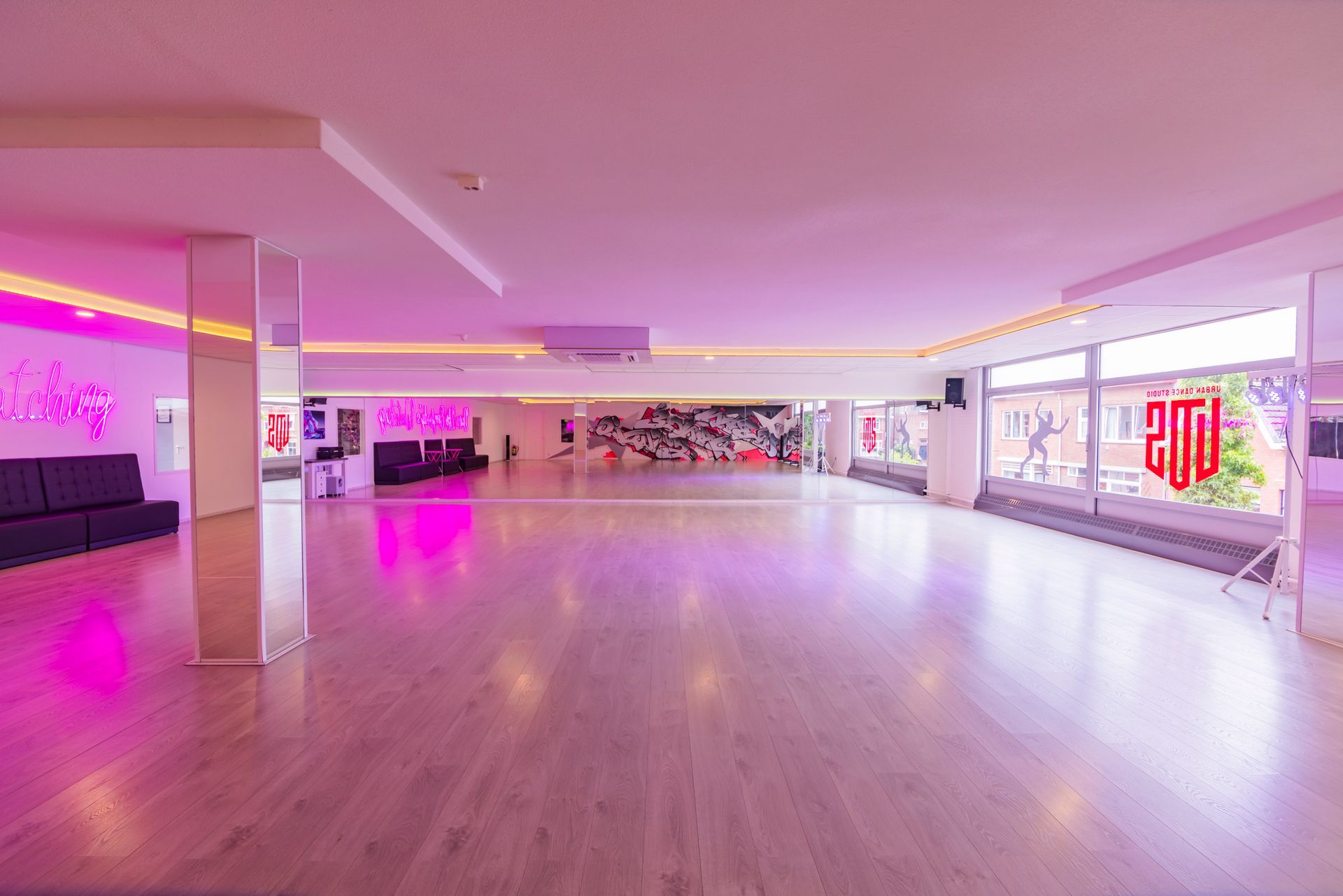 Een lege dansstudio met roze verlichting, spiegelwanden en gepolijste houten vloeren.