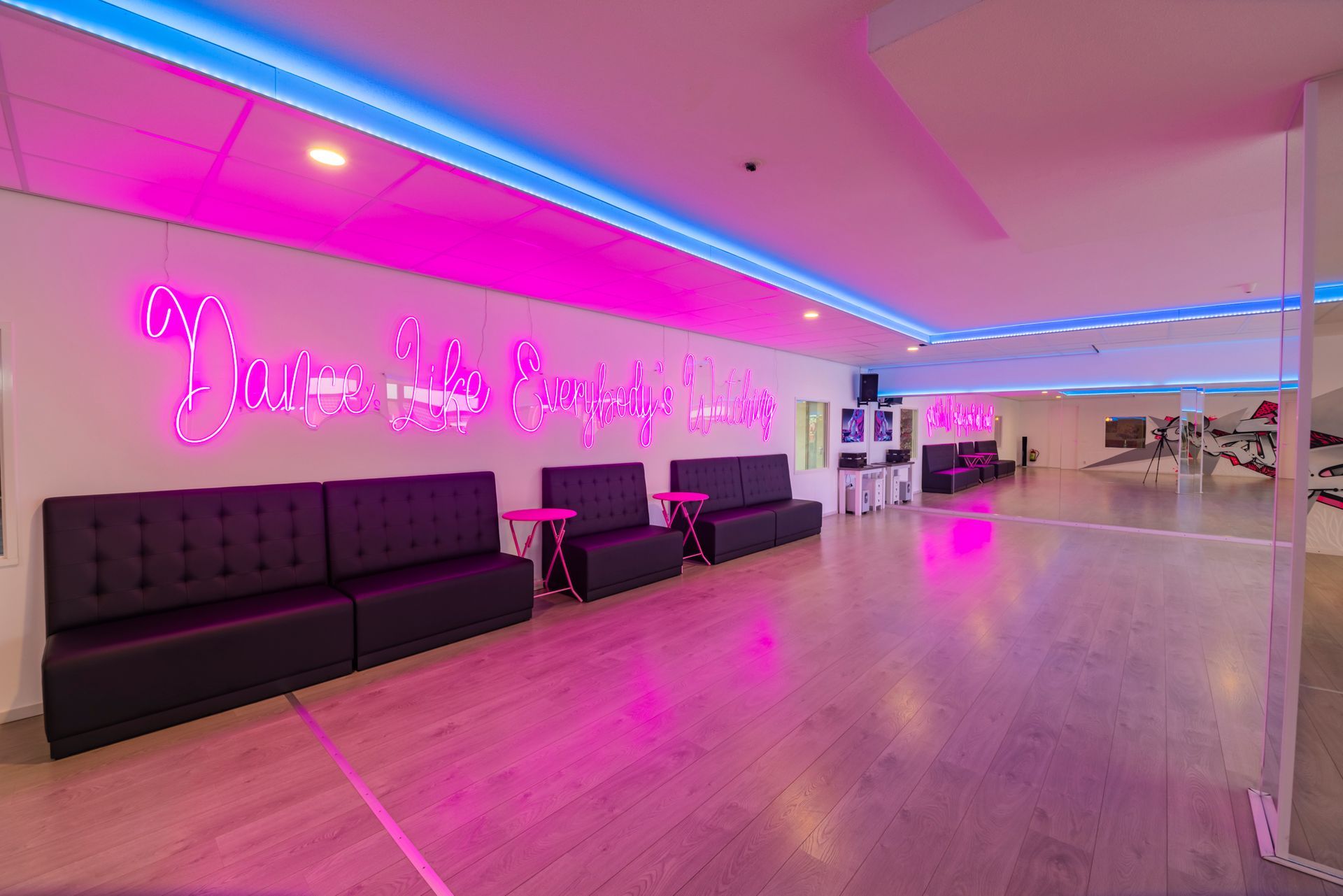 Een lounge verlicht in neonroze met zwarte zitmeubels, roze reflecties in de vloer en kunstwerken 