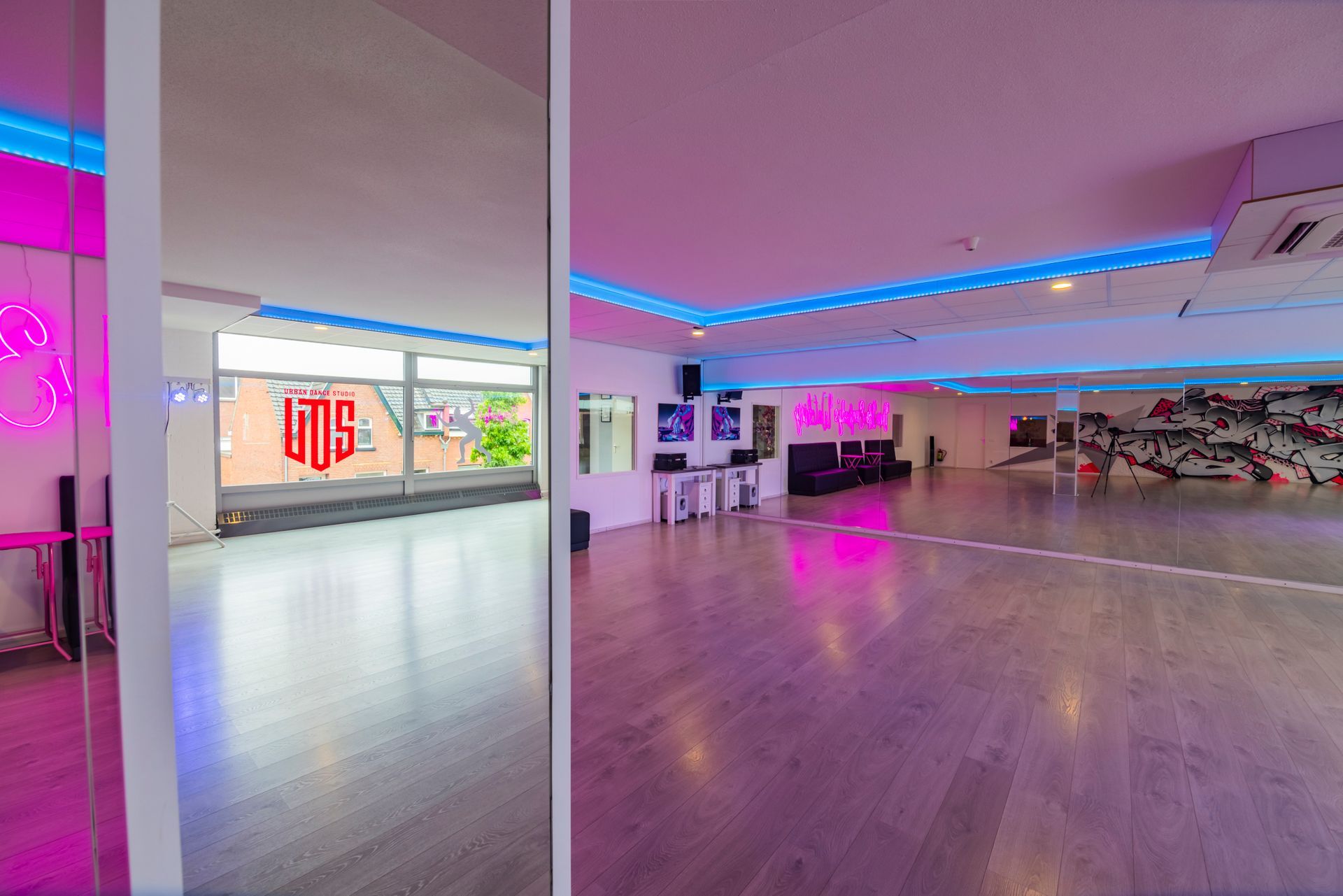 Een lichte, lege dansstudio met spiegels, neonroze-blauwe verlichting en gepolijste houten vloeren.
