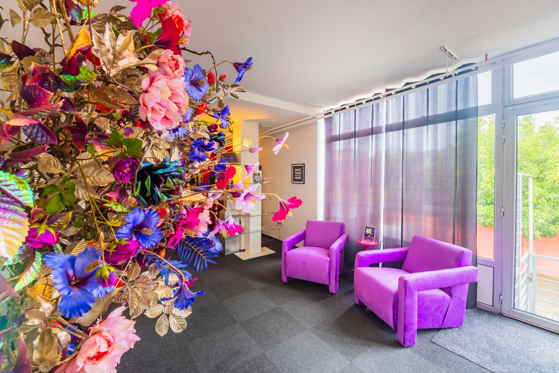 Lobby met een grote, kleurrijke bloemenwand en twee paarse stoelen bij hoge ramen.
