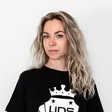 Vrouw met golvend blond haar in een zwarte sweater tegen een witte achtergrond.