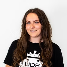 Vrouw met lang bruin haar lacht in een zwart shirt tegen een witte achtergrond.