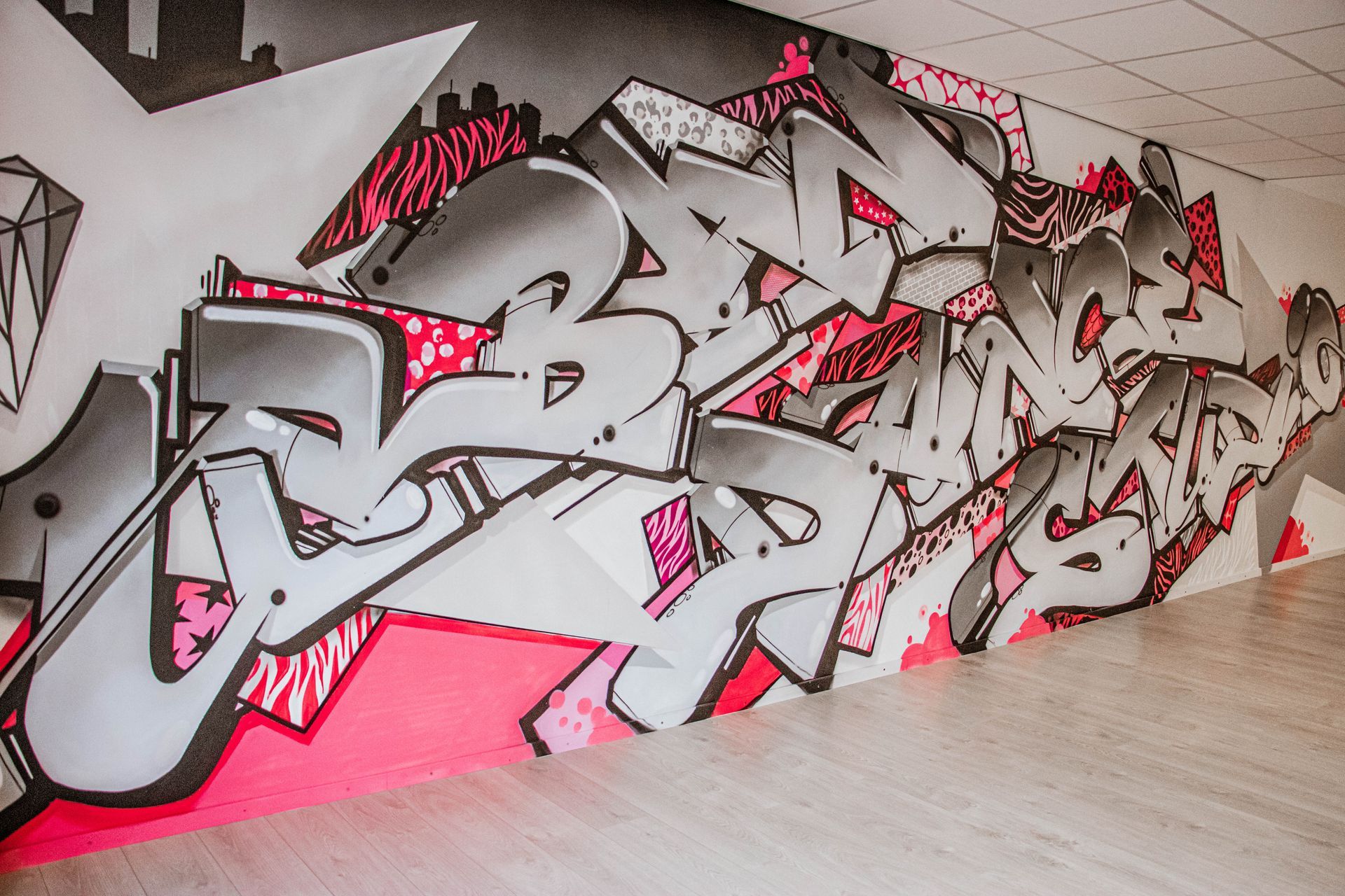 Een graffiti-muurschildering in roze, grijs en zwart op een muur in een gang.