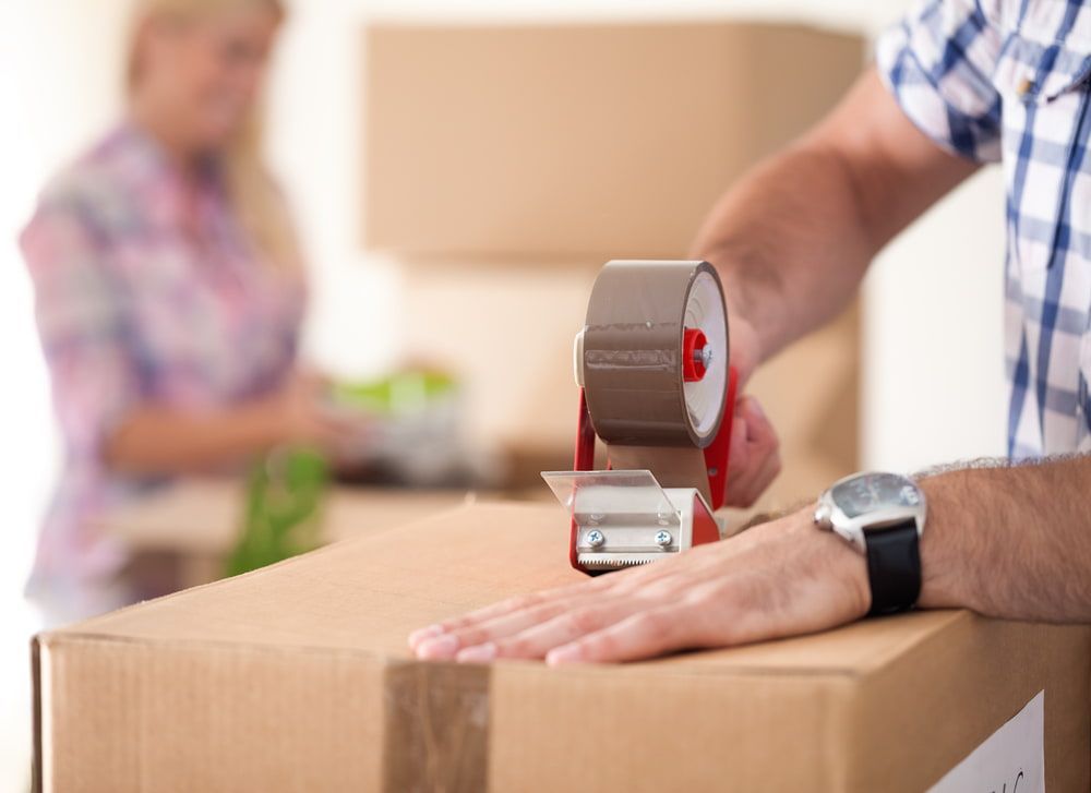 A Man Is Taping A Cardboard Box With Brown Tape — Fairdinkum Removals In Nowra, NSW